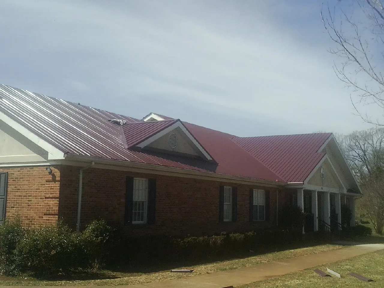 Red metal roof with gabled entries on a long brick building, from a Hail Damage Roof Repair job in Kaysville