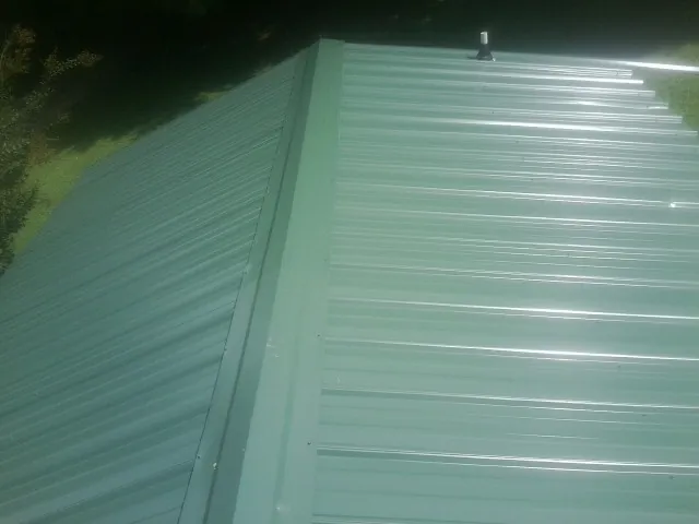 New green metal panels meeting at the ridge of a roof — Flat Roof Repair work by our crew in Kaysville