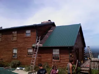 Green metal roof going on a two story log home with ladders set in Kaysville