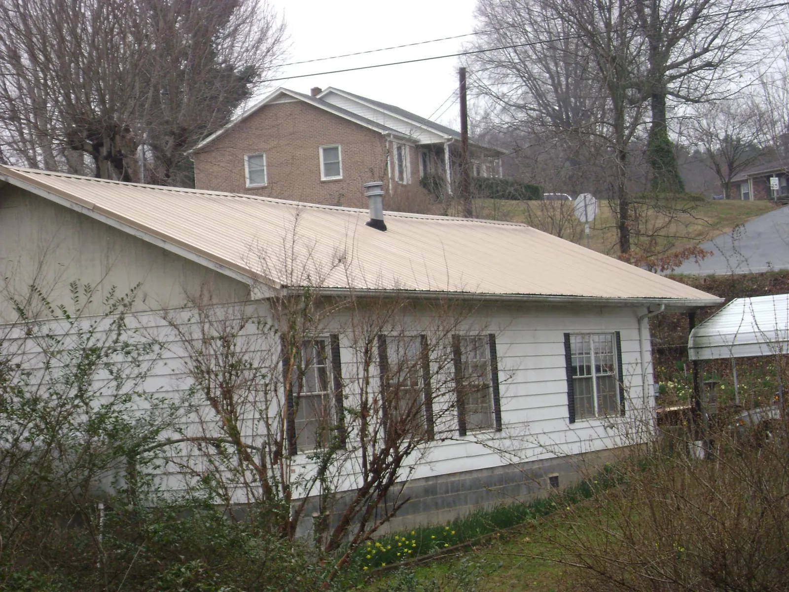 Tan metal roof on a white sided house set into a hillside — Commercial Roofing by Roofing Brothers in Kaysville